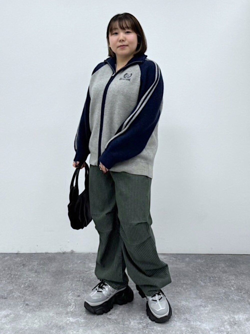 ブルー系のニット/セーター、ブラック系のハンドバッグ、グリーン系のデニムパンツを着用したレディースの秋コーディネートの1枚目の写真