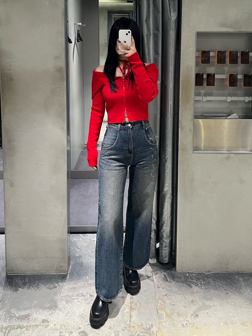 レッド系のニット/セーター、ブルー系のデニムパンツ、ブラック系のブーツを着用したレディースの秋コーディネートの1枚目の写真