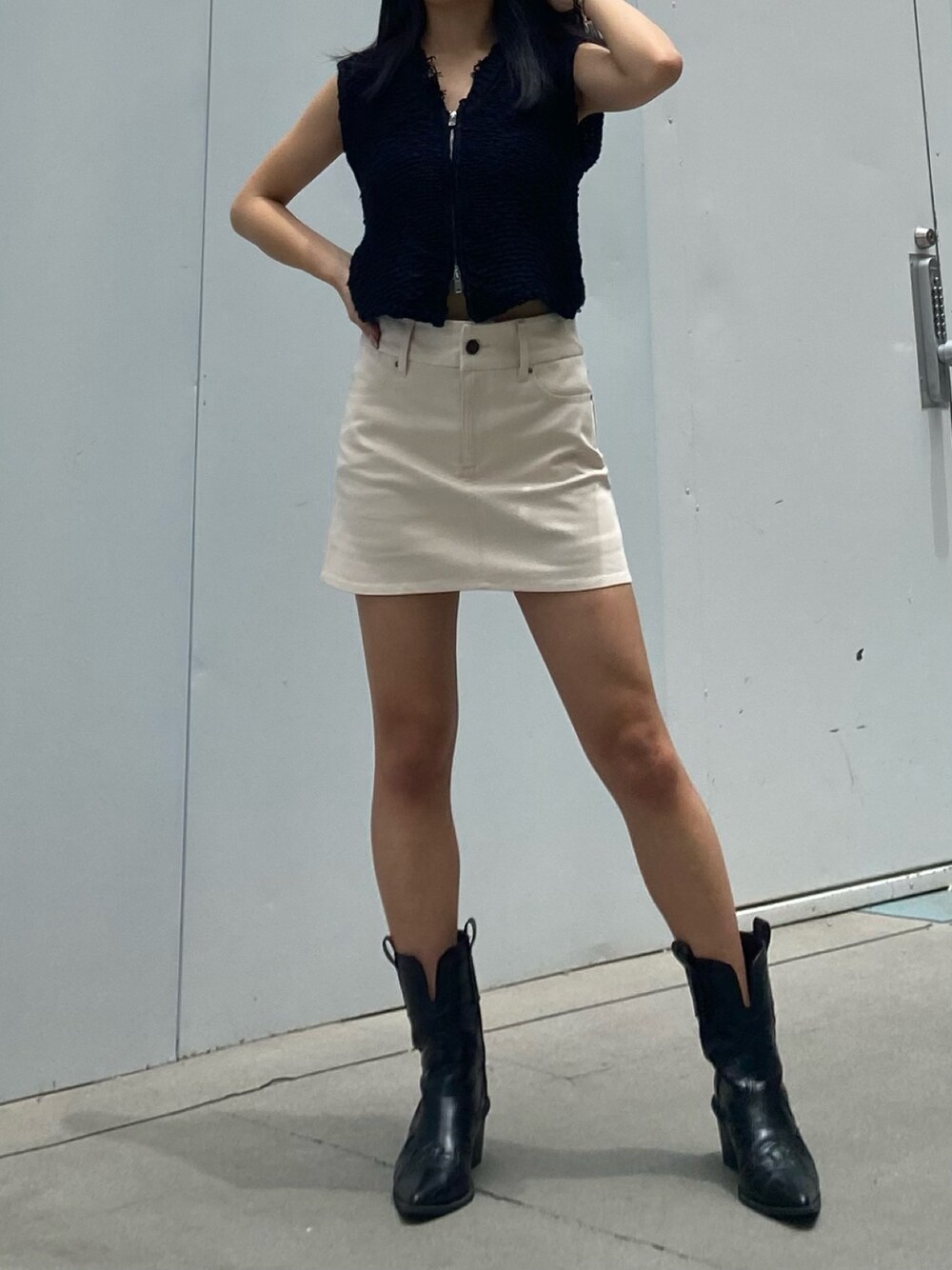 ホワイト系のベスト、ホワイト系のスカート、ブラック系のブーツを着用したレディースの夏コーディネートの1枚目の写真