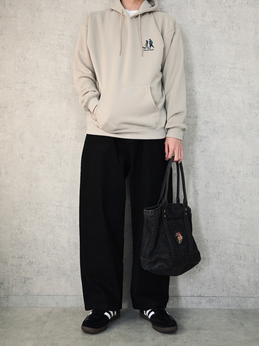 ベージュ系のパーカー、ブラック系のトートバッグ、ブラック系のスニーカーを着用したメンズの春コーディネートの1枚目の写真