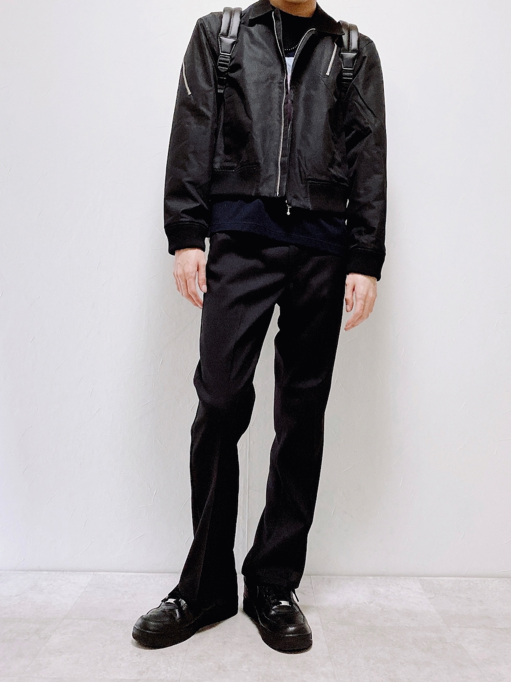 ブラック系のブルゾン、ブラック系のスラックス、ブラウン系のバックパック/リュックを着用したメンズの春コーディネートの1枚目の写真