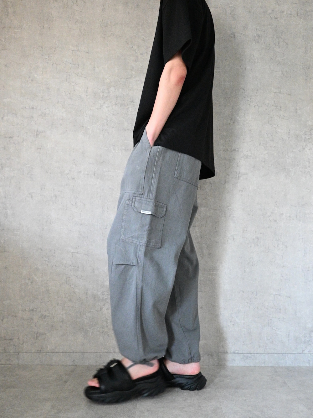 グレー系のカーゴパンツ、ブラック系のTシャツ/カットソー、ブラック系のサンダルを着用したメンズの夏コーディネートの1枚目の写真