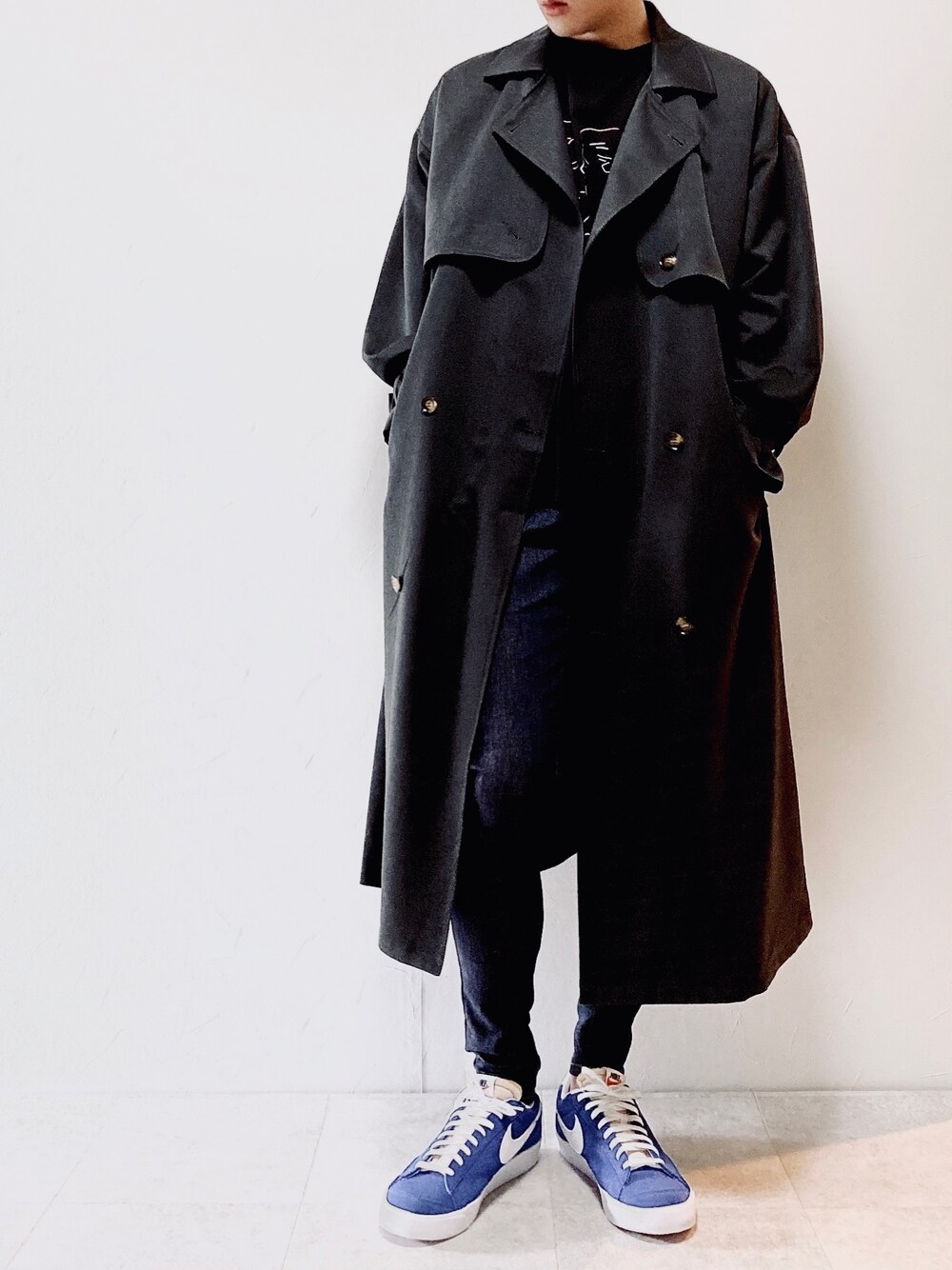 グレー系のトレンチコート、ブラック系のTシャツ/カットソー、ブルー系のデニムパンツを着用したメンズの秋コーディネートの1枚目の写真