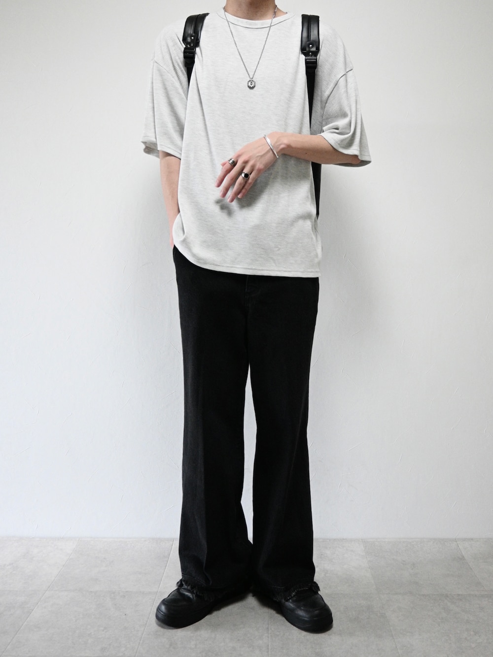 ブラック系のデニムパンツ、ベージュ系のTシャツ/カットソー、シルバー系のネックレスを着用したメンズの春コーディネートの1枚目の写真