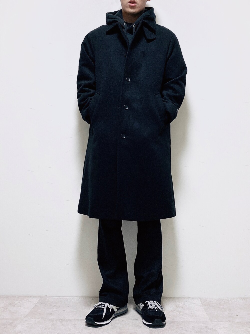 ブラック系のステンカラーコート、ブラック系のスラックス、ブラック系のスニーカーを着用したメンズの冬コーディネートの1枚目の写真