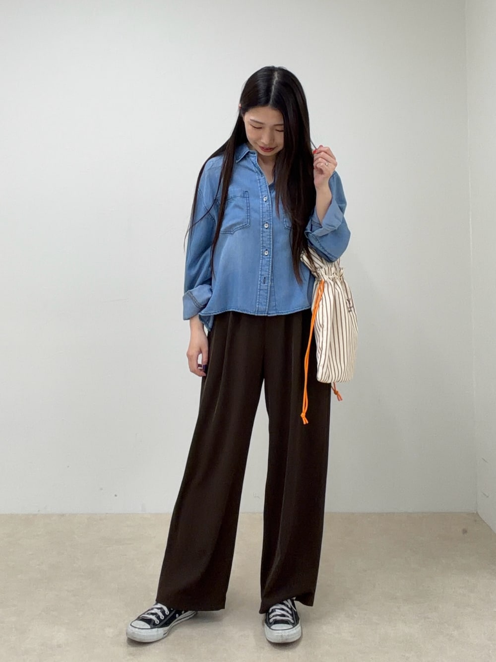 ブルー系のシャツ/ブラウス、ブラウン系のスラックス、レッド系のトートバッグを着用したレディースの春コーディネートの1枚目の写真