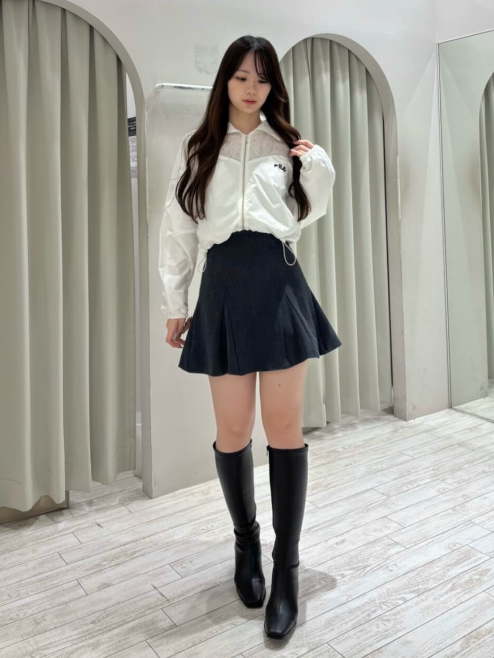 ブラック系のブーツ、ホワイト系のナイロンジャケット、グレー系のスカートを着用したレディースの冬コーディネートの1枚目の写真