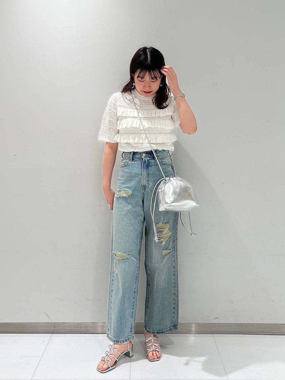 シルバー系のサンダル、シルバー系のショルダーバッグ、ブルー系のデニムパンツを着用したレディースの春コーディネートの1枚目の写真