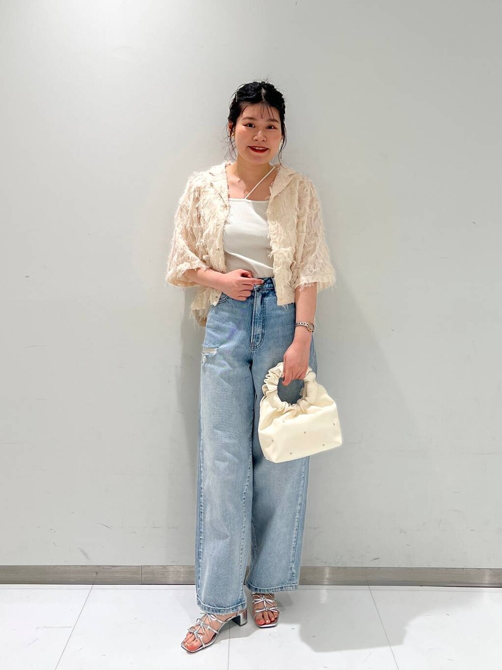 ブルー系のデニムパンツ、ベージュ系のハンドバッグ、ホワイト系のキャミソールを着用したレディースの夏コーディネートの1枚目の写真