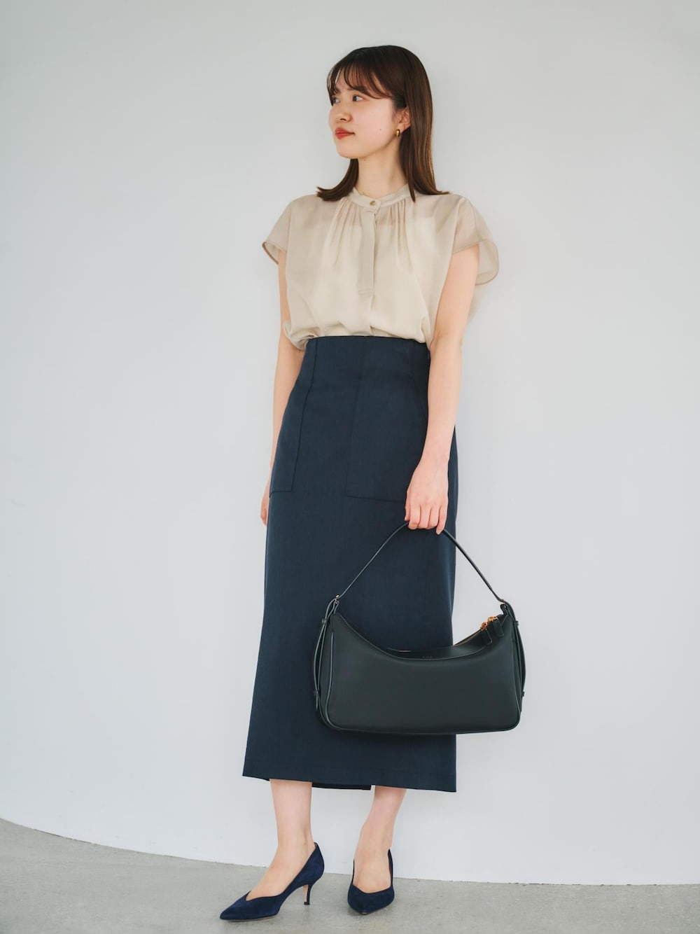 ブルー系のスカート、ブラック系のハンドバッグ、ベージュ系のシャツ/ブラウスを着用したレディースの春コーディネートの1枚目の写真