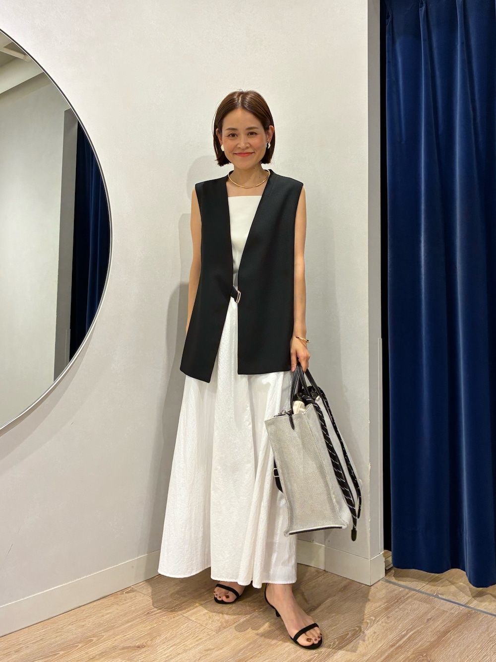 ブラック系のベスト、ホワイト系のキャミソール、ホワイト系のスカートを着用したレディースの夏コーディネートの1枚目の写真