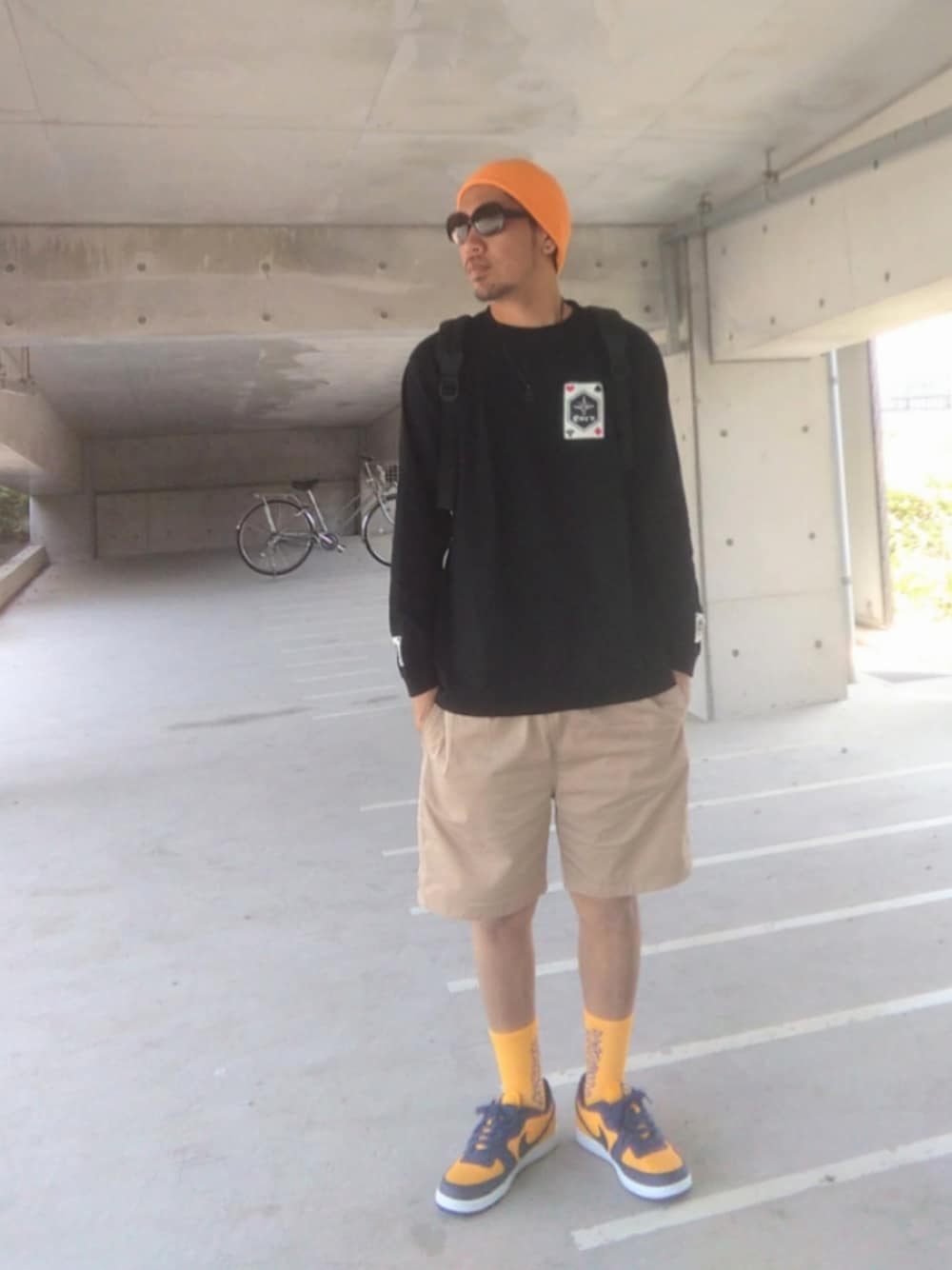 ブラック系のTシャツ/カットソー、ベージュ系のチノパンツ、ブラック系のバックパック/リュックを着用したメンズの春コーディネートの1枚目の写真