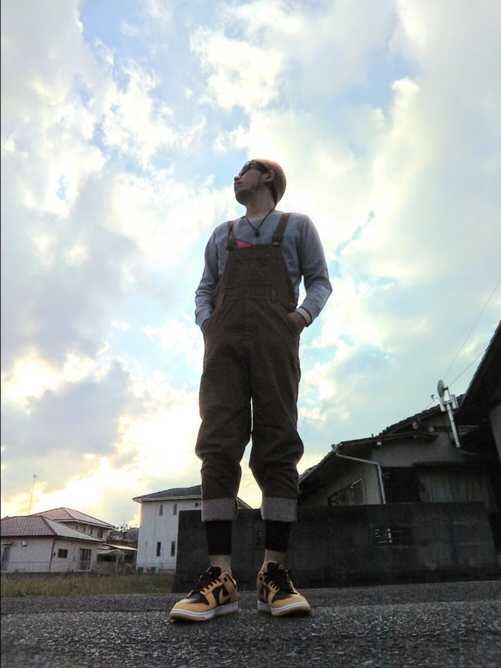 グレー系のスウェット、ブラウン系のサロペット/オーバーオール、イエロー系のスニーカーを着用したメンズの秋コーディネートの1枚目の写真