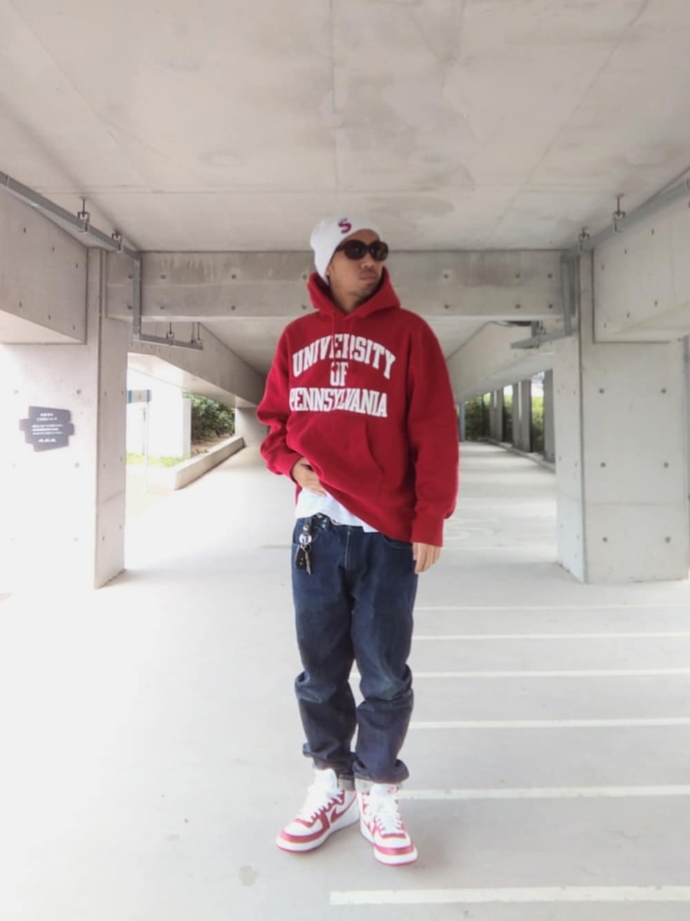 レッド系のパーカー、ブルー系のデニムパンツ、ホワイト系のスニーカーを着用したメンズの冬コーディネートの1枚目の写真