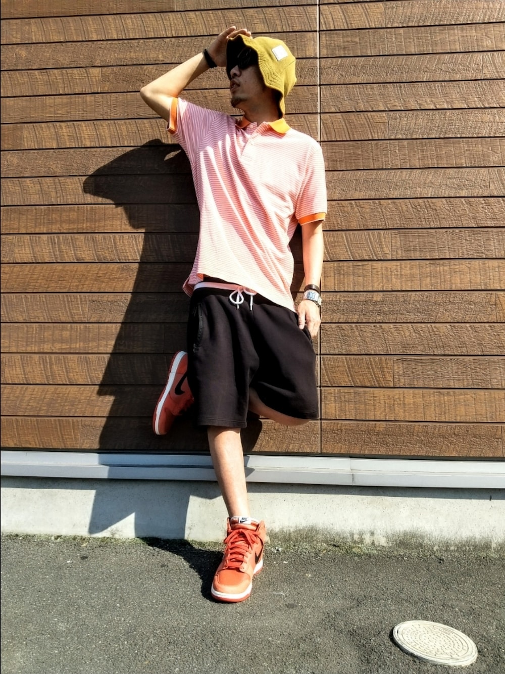 オレンジ系のポロシャツ、ブラック系のその他パンツ、オレンジ系のスニーカーを着用したメンズの夏コーディネートの1枚目の写真