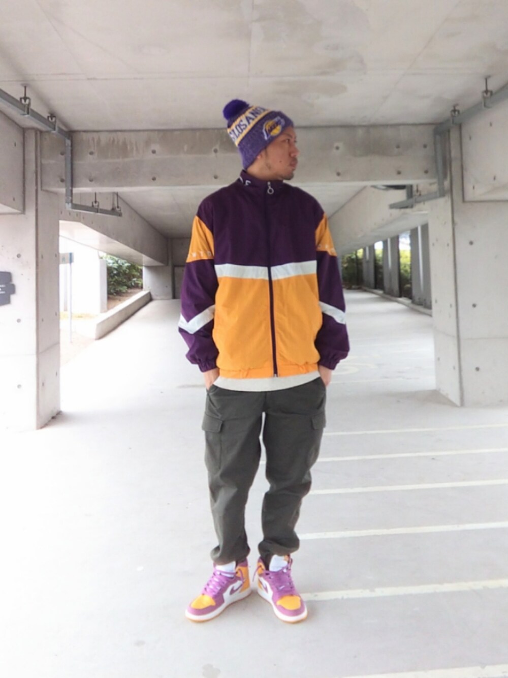 パープル系のナイロンジャケット、グリーン系のカーゴパンツ、イエロー系のスニーカーを着用したメンズの春コーディネートの1枚目の写真