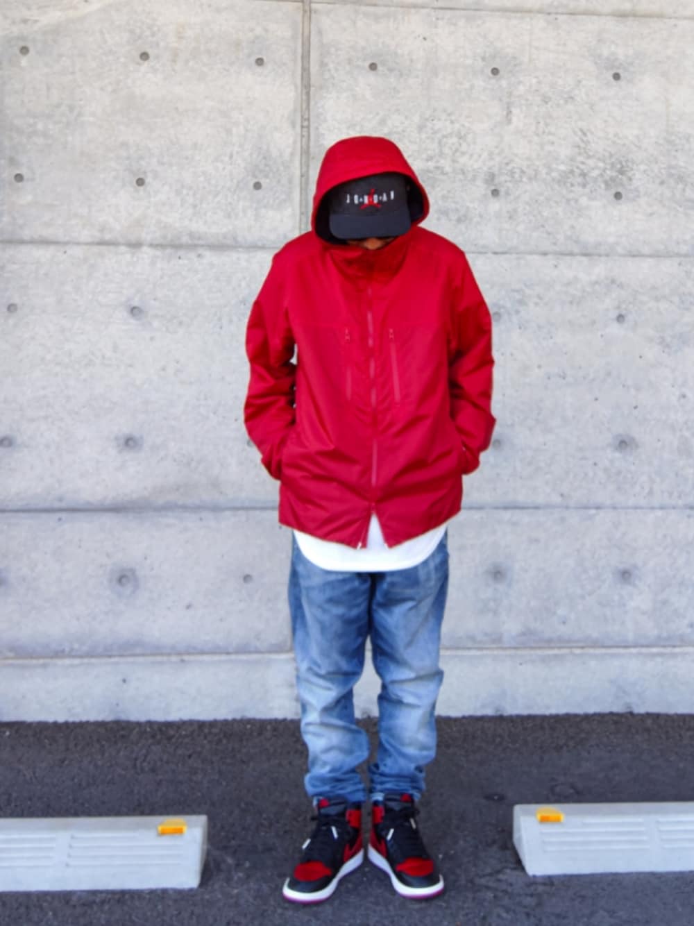 レッド系のナイロンジャケット、ホワイト系のタンクトップ、ブルー系のデニムパンツを着用したメンズの秋コーディネートの1枚目の写真