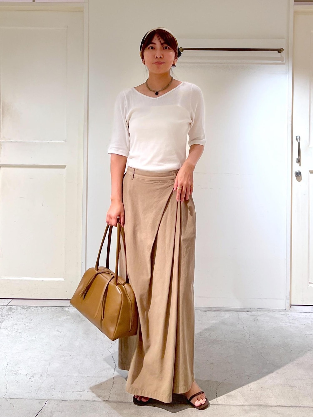 ブラウン系のハンドバッグ、ブラウン系のサンダル、ホワイト系のTシャツ/カットソーを着用したレディースの夏コーディネートの1枚目の写真