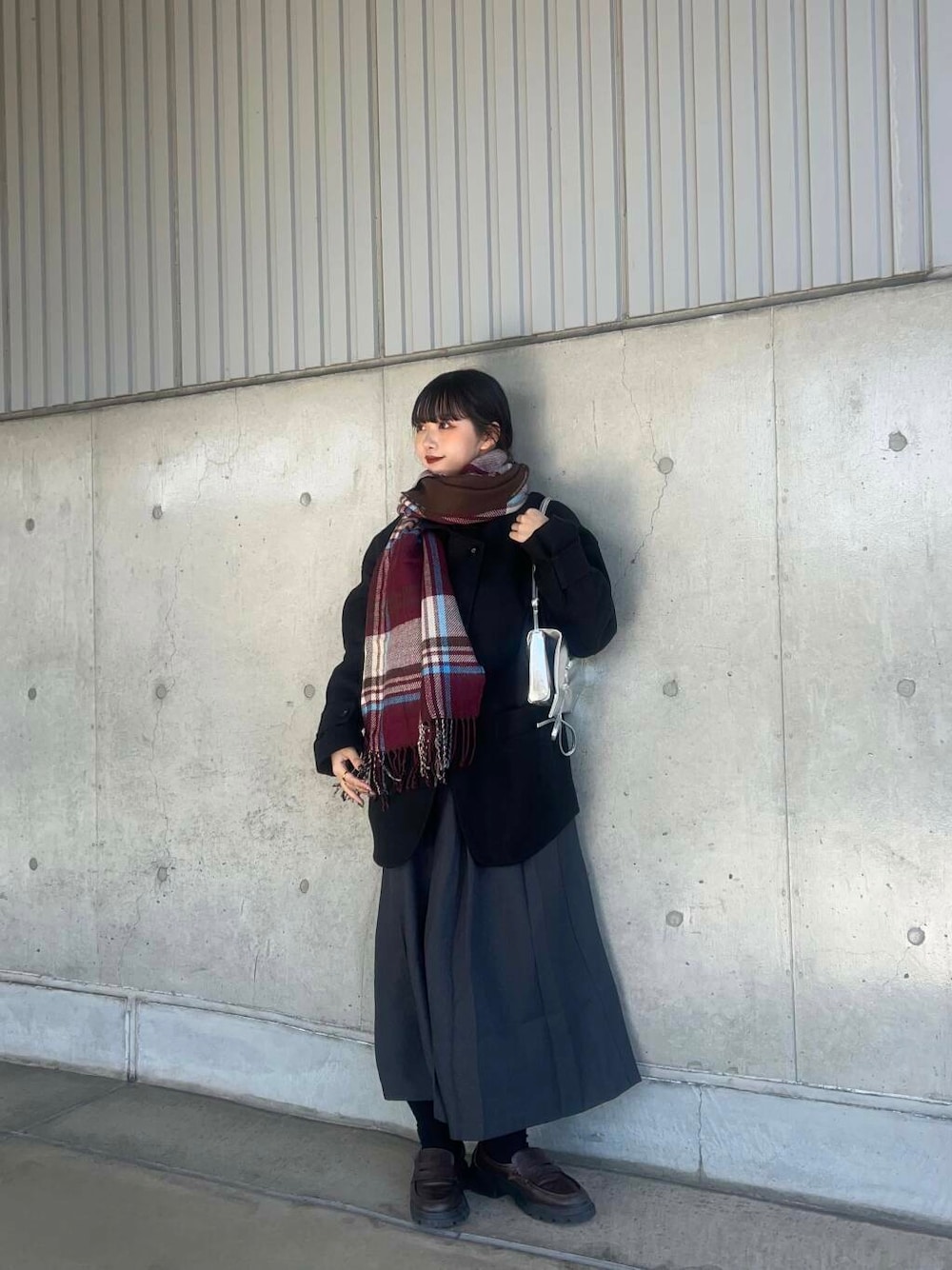 ブラック系のステンカラーコート、グレー系のワンピース、シルバー系のショルダーバッグを着用したレディースの冬コーディネートの1枚目の写真