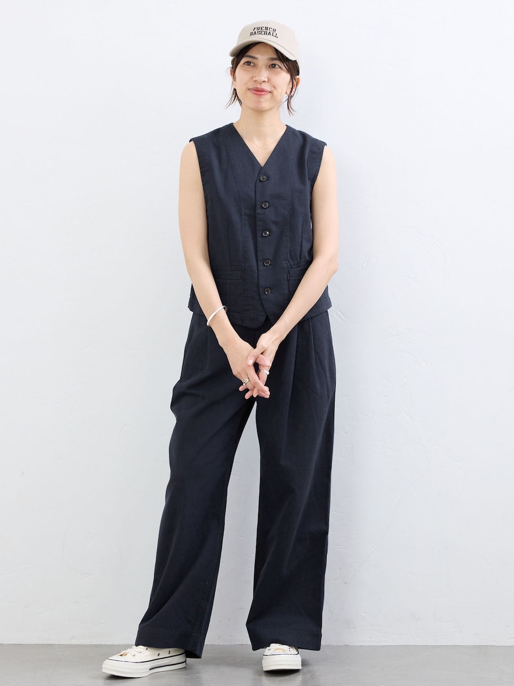 ブルー系のベスト、ブルー系のチノパンツ、ベージュ系のキャップを着用したレディースの夏コーディネートの1枚目の写真