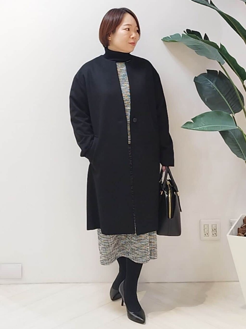 ブラック系のノーカラーコート、ブラック系のTシャツ/カットソー、ブラック系のスカートを着用したレディースの秋コーディネートの1枚目の写真