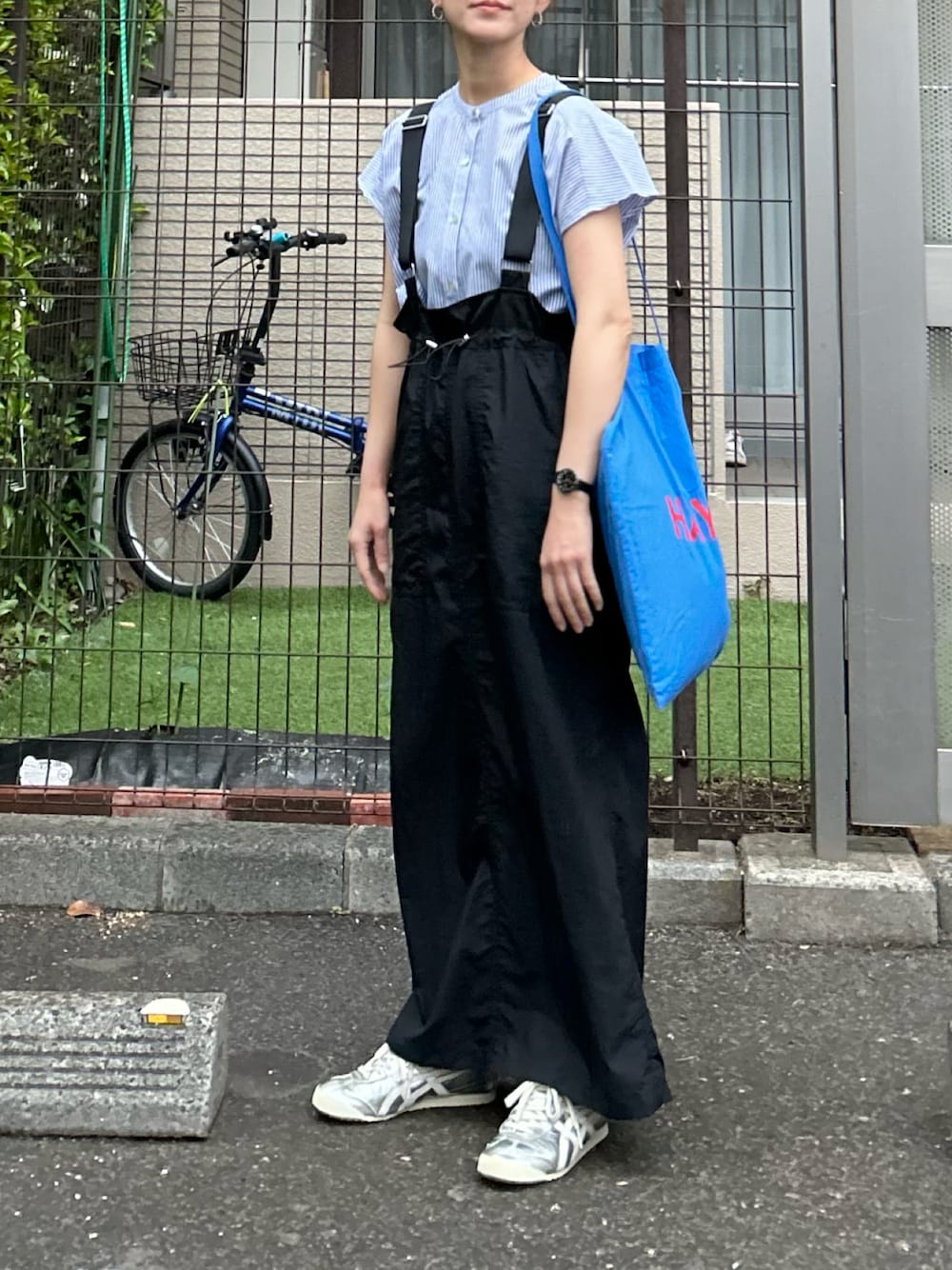 ブルー系のシャツ/ブラウス、ブラック系のジャンパースカート、シルバー系のスニーカーを着用したレディースの春コーディネートの1枚目の写真