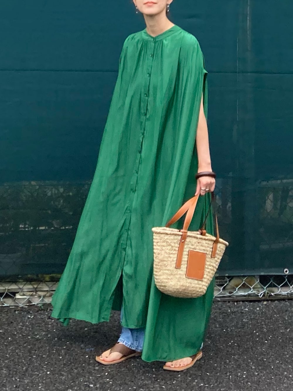 グリーン系のシャツワンピース、ブラウン系のかごバッグ、ブルー系のデニムパンツを着用したレディースの夏コーディネートの1枚目の写真