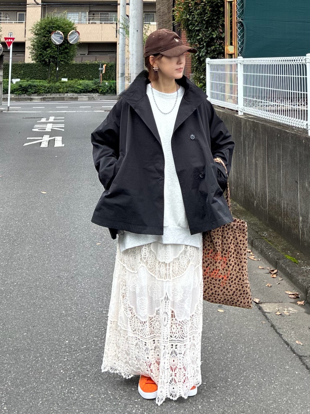 オレンジ系のスニーカー、ホワイト系のスカート、ブラック系のトレンチコートを着用したレディースの秋コーディネートの1枚目の写真