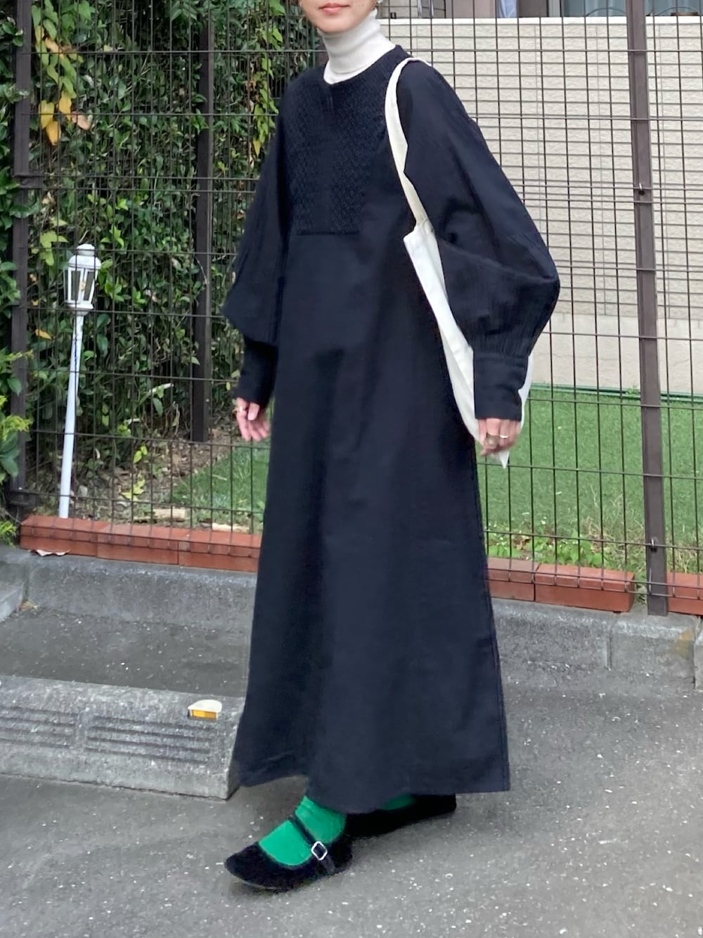 ブラック系のワンピース、ホワイト系のトートバッグ、ゴールド系のピアス（両耳用）を着用したレディースの秋コーディネートの1枚目の写真