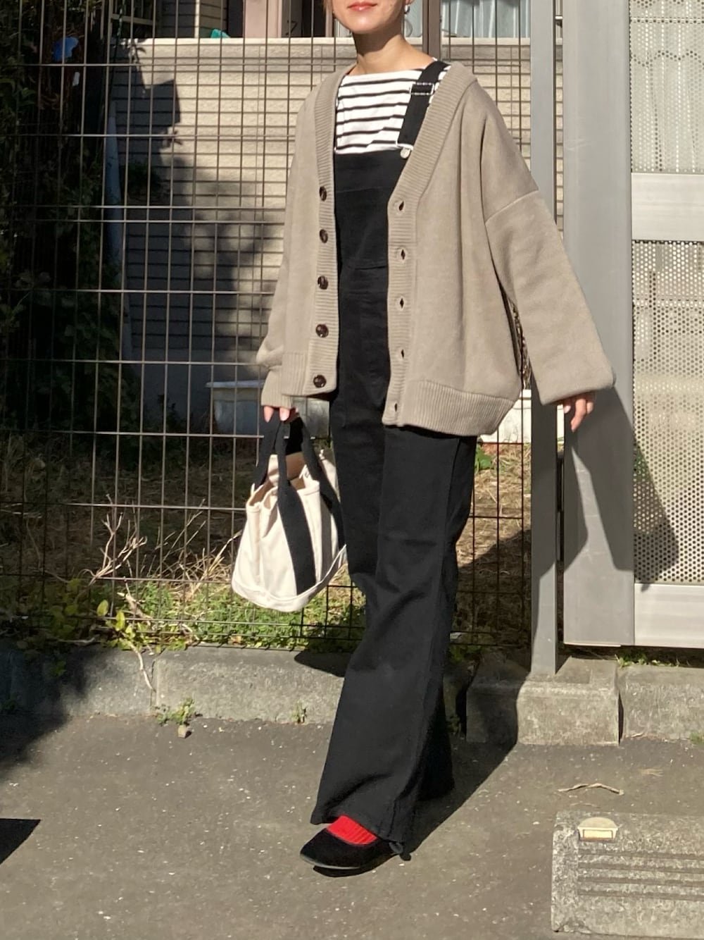 ベージュ系のカーディガン/ボレロ、ブラック系のサロペット/オーバーオール、ホワイト系のトートバッグを着用したレディースの冬コーディネートの1枚目の写真