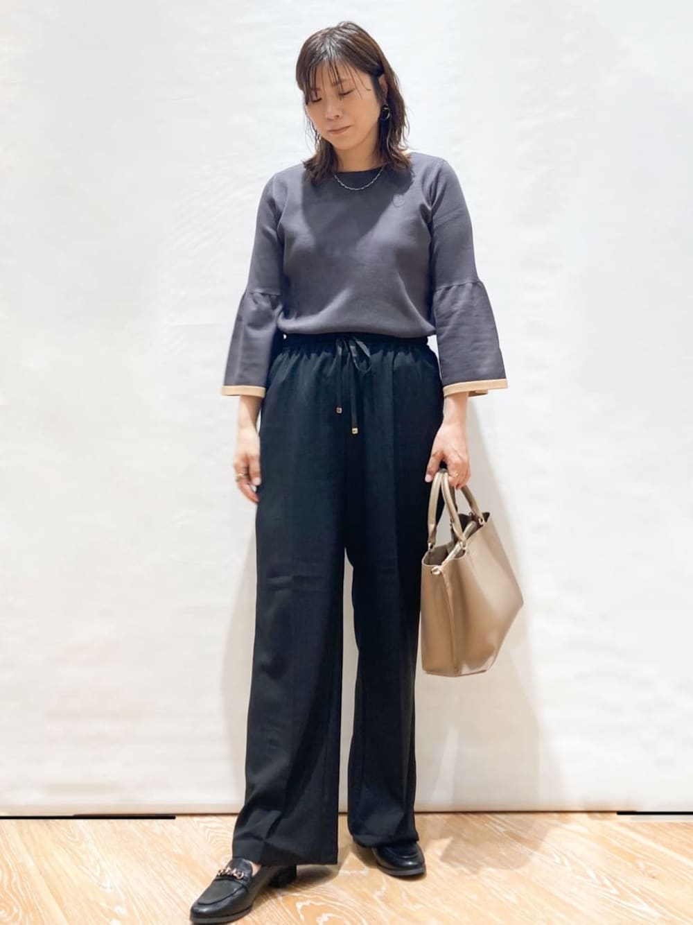 グレー系のニット/セーター、ブラック系のその他パンツ、ベージュ系のトートバッグを着用したレディースの秋コーディネートの1枚目の写真