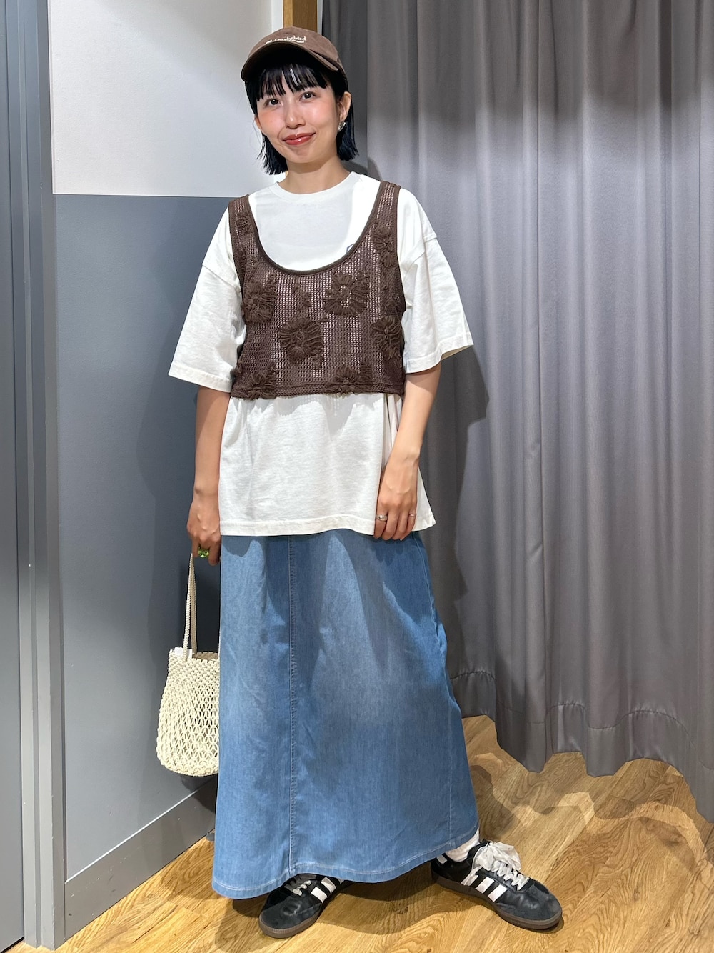 ブラウン系のベスト、ブルー系のスカート、ブラウン系のキャップを着用したレディースの夏コーディネートの1枚目の写真