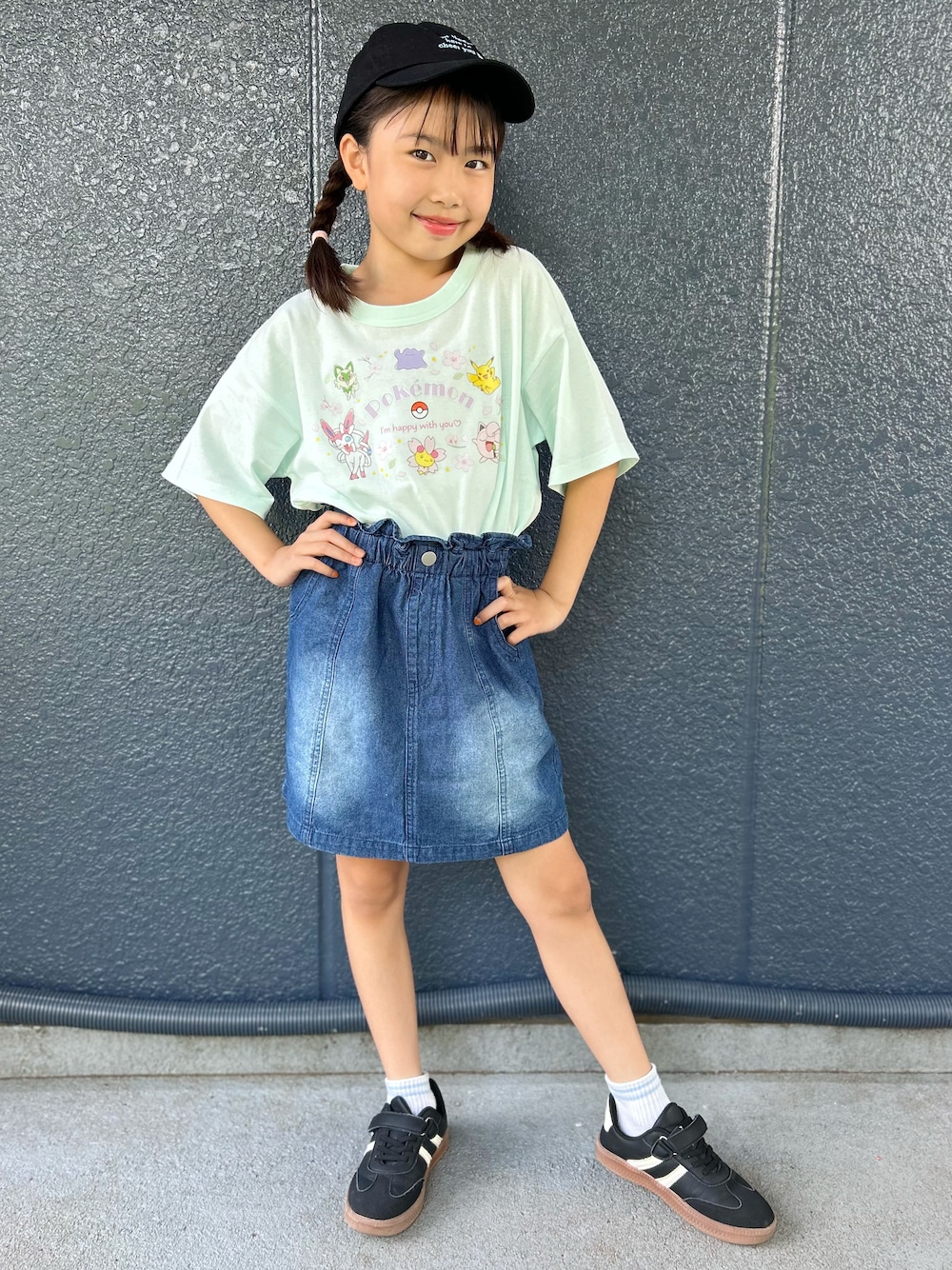 グリーン系のTシャツ/カットソー、ブルー系のデニムスカート、ブラック系のキャップを着用したキッズの夏コーディネートの1枚目の写真