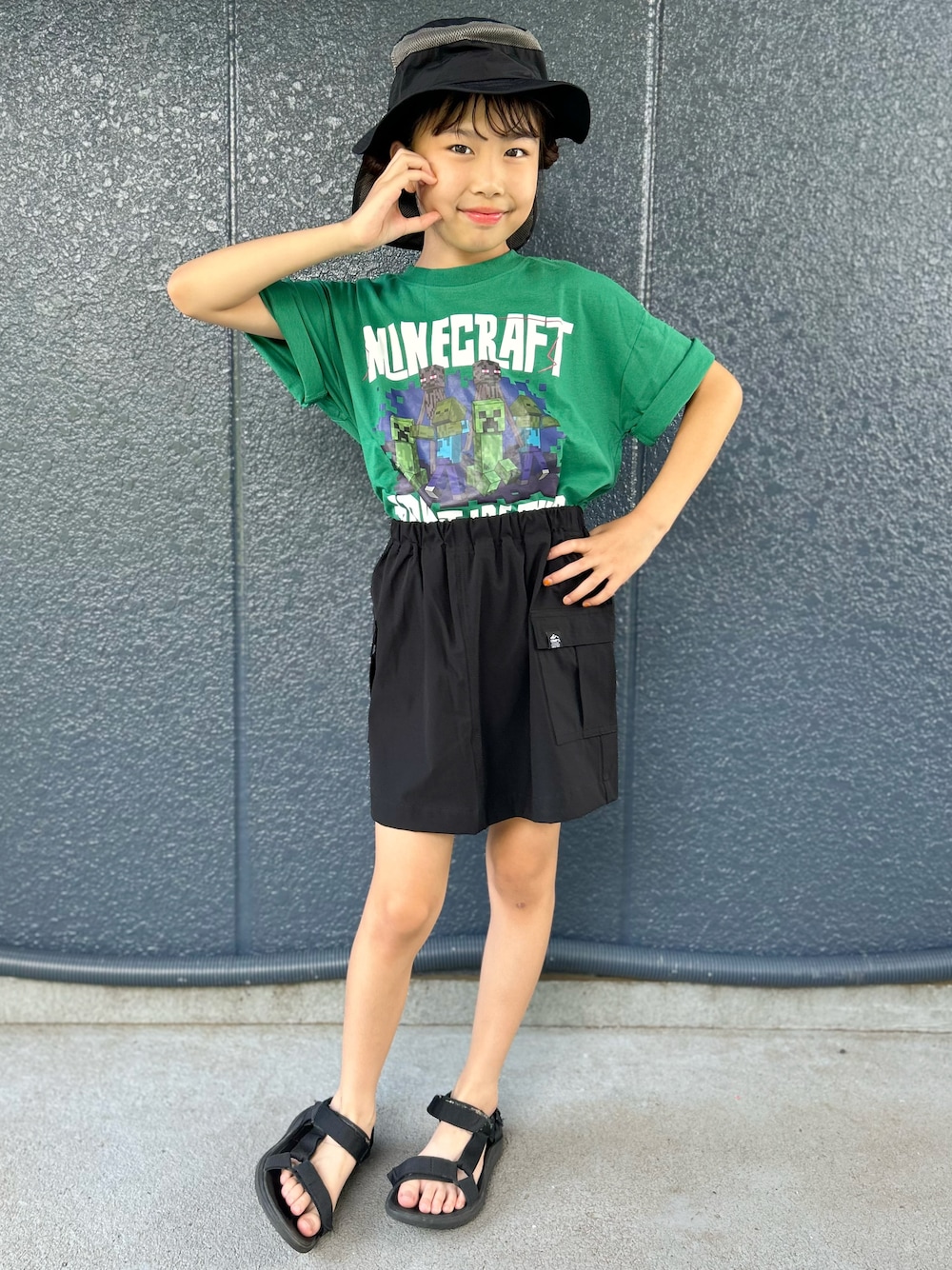 グリーン系のTシャツ/カットソー、ブラック系のスカート、ブラック系のハットを着用したキッズの夏コーディネートの1枚目の写真