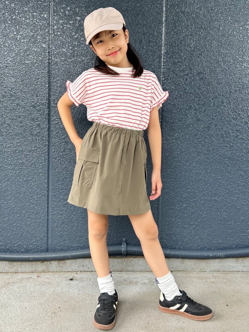 レッド系のTシャツ/カットソー、ブラウン系のスカート、ベージュ系のキャップを着用したキッズの夏コーディネートの1枚目の写真