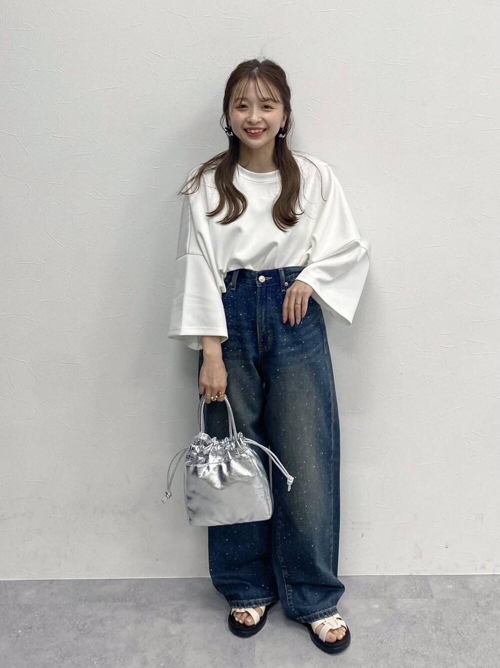 ブルー系のデニムパンツ、ホワイト系のスニーカー、シルバー系のハンドバッグを着用したレディースの春コーディネートの1枚目の写真
