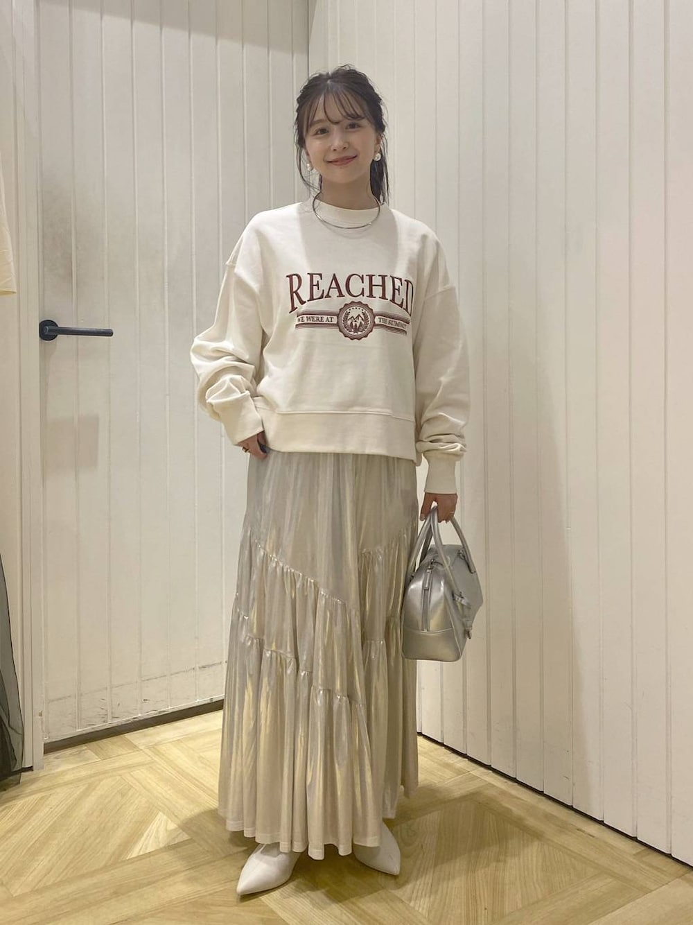 ホワイト系のスウェット、シルバー系のボストンバッグ、ホワイト系のブーツを着用したレディースの秋コーディネートの1枚目の写真