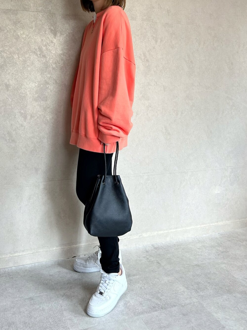 オレンジ系のスウェット、ブラック系のショルダーバッグ、ホワイト系のスニーカーを着用したレディースの春コーディネートの1枚目の写真