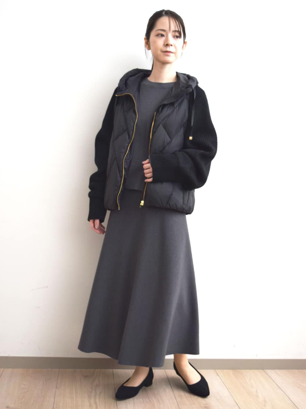 ブラック系のダウンジャケット/コート、グレー系のニット/セーター、グレー系のスカートを着用したレディースの秋コーディネートの1枚目の写真