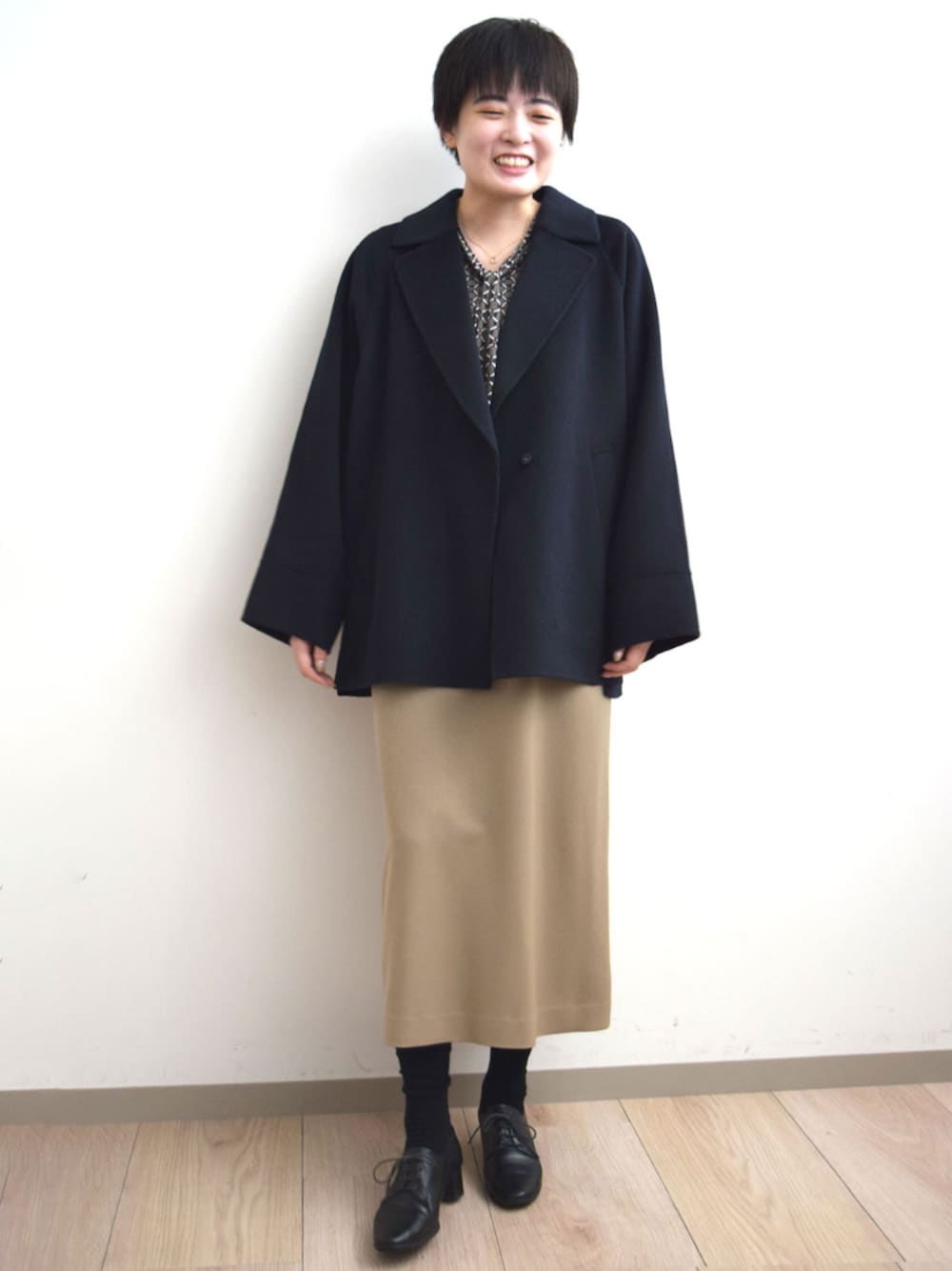 ベージュ系のジャンパースカート、ブラウン系のTシャツ/カットソー、ブルー系のノーカラーコートを着用したレディースの秋コーディネートの1枚目の写真