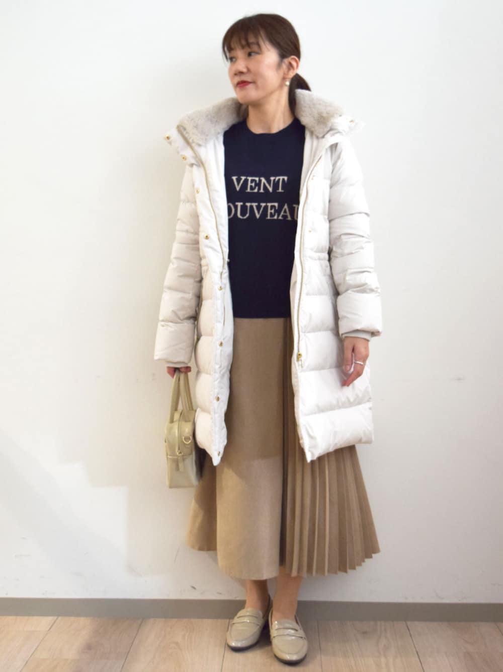 ベージュ系のスカート、ホワイト系のダウンジャケット/コート、ブルー系のニット/セーターを着用したレディースの秋コーディネートの1枚目の写真