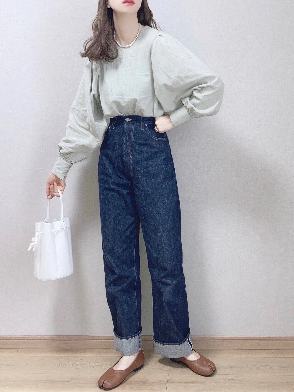 ブルー系のデニムパンツ、ホワイト系のバッグ、ブラウン系のパンプスを着用したレディースの冬コーディネートの1枚目の写真