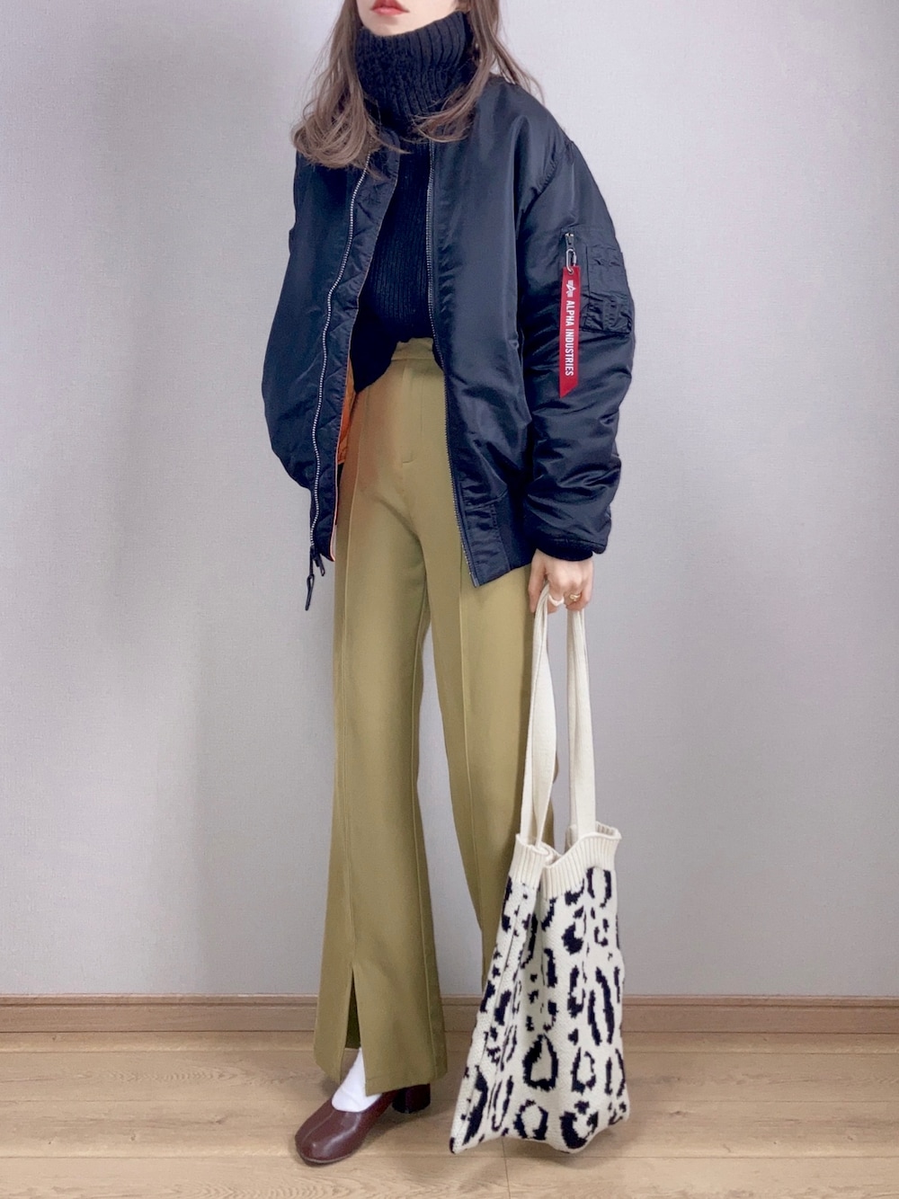 ブラック系のMA-1、グリーン系のスラックス、ホワイト系のトートバッグを着用したレディースの冬コーディネートの1枚目の写真