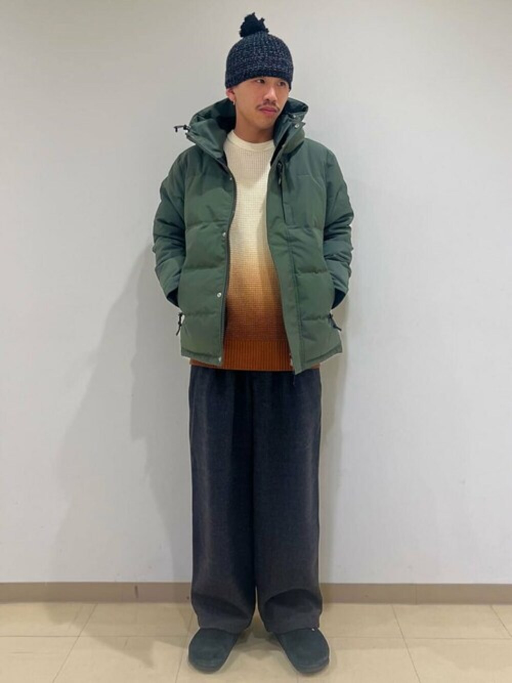 グリーン系のダウンジャケット/コート、オレンジ系のニット/セーター、ブラック系のその他パンツを着用したメンズの冬コーディネートの1枚目の写真
