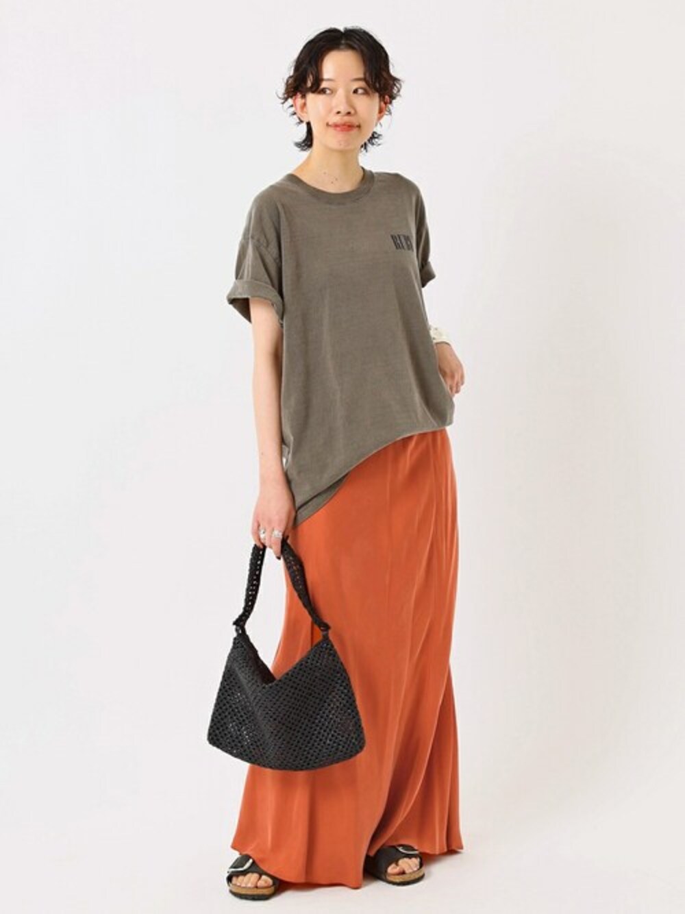 オレンジ系のスカート、ブラック系のハンドバッグ、ブラック系のサンダルを着用したレディースの夏コーディネートの1枚目の写真