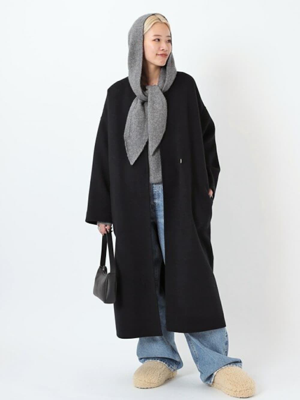 グレー系のニット/セーター、ブラック系のノーカラーコート、ブルー系のデニムパンツを着用したレディースの秋コーディネートの1枚目の写真