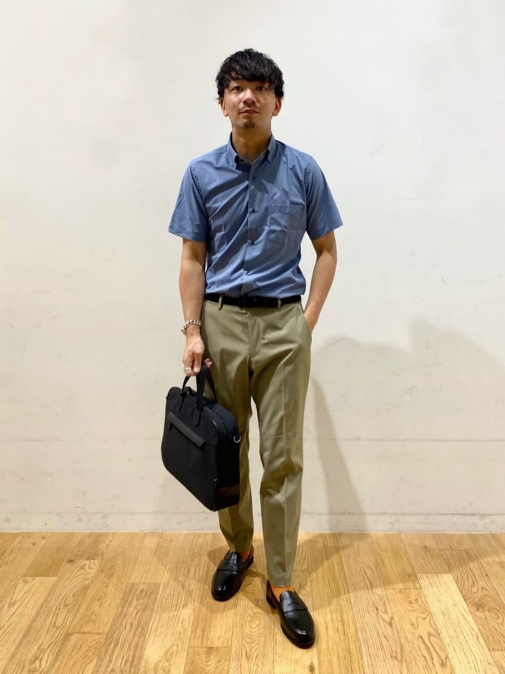 ブルー系のビジネスシャツ、ブラウン系のスラックス、ブラック系のビジネスバッグを着用したメンズの夏コーディネートの1枚目の写真