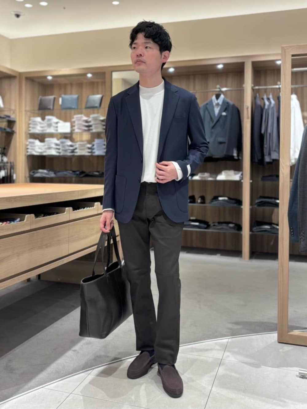 ブラウン系のトートバッグ、ブルー系のテーラードジャケット、ホワイト系のTシャツ/カットソーを着用したメンズの秋コーディネートの1枚目の写真