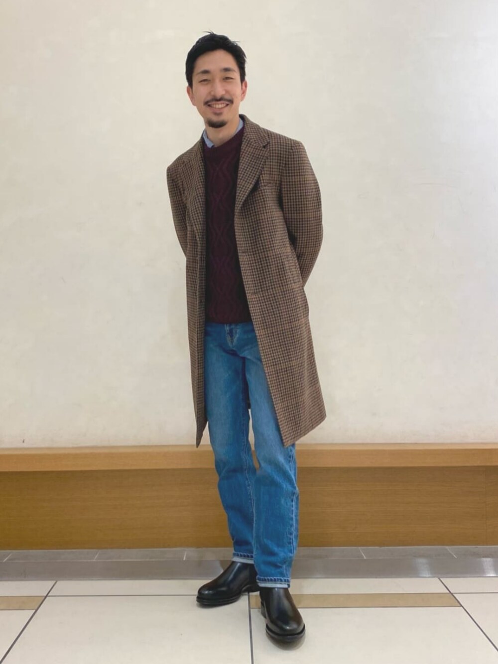 ブラウン系のチェスターコート、ブルー系のデニムパンツ、レッド系のニット/セーターを着用したメンズの冬コーディネートの1枚目の写真