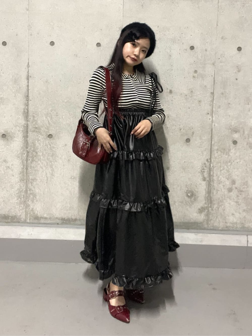 レッド系のハンドバッグ、レッド系のパンプス、ブラック系のスカートを着用したレディースの秋コーディネートの1枚目の写真